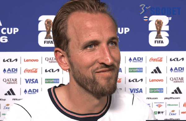Man with blond hair and beard at a FIFA World Cup press conference, sponsor logos on the backdrop behind him.